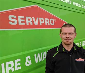 Male employee AJ standing in front of green SERVPRO van