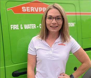 Female employee Katie standing in front of green SERVPRO vehicle
